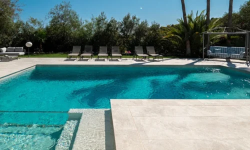 Piscina con jardín y tumbonas usando azulejos baratos para piscinas en tonos claros Piscina con jardín y tumbonas usando azulejos baratos para piscinas en tonos claros