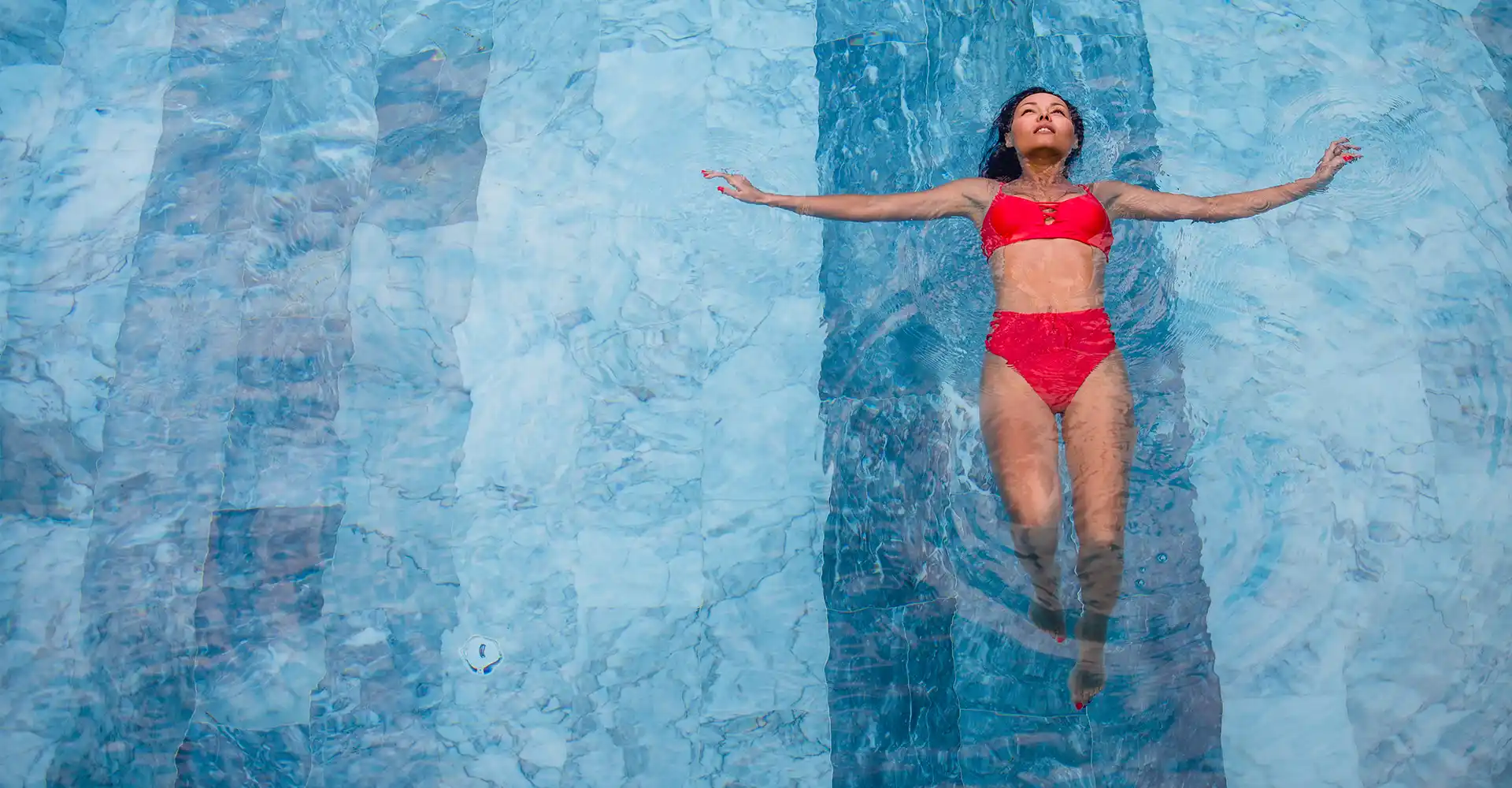 Mujer relajada sobre el agua con porcelanico para piscina en tonos azules Mujer relajada sobre el agua con porcelanico para piscina en tonos azules